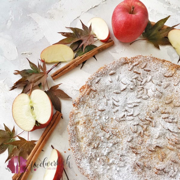 Klassische Torta della Nonna mit Apfel. Fotografiert mit rotem Herbstlaub und geschnittenen Äpfeln.