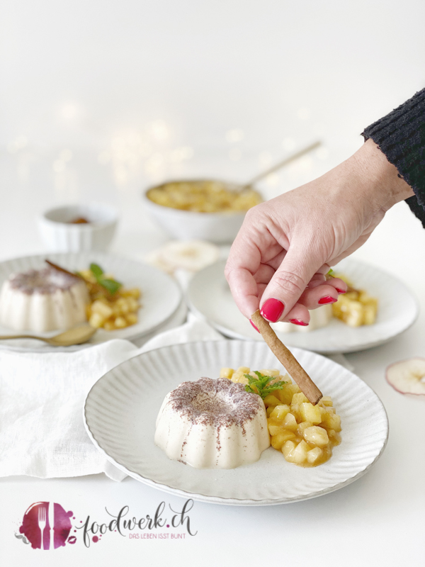 Hand mit Zimtstange und Zimt Panna Cotta mit Bratapfel Kompott