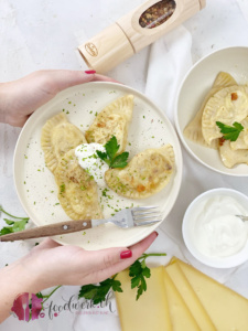 Pierogi gefüllt mir Raclettekäse und Kartoffeln werden auf einem Teller serviert