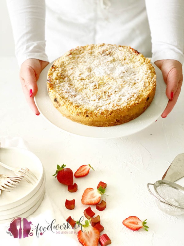 Der Streuselkuchen mit Erdbeeren und Rhabarber wird auf weisser Tortenplatte serviert