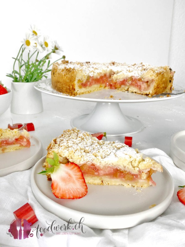 Streuselkuchen mit Erdbeeren und Rhabarber angeschnitten auf Teller und Tortenplatte