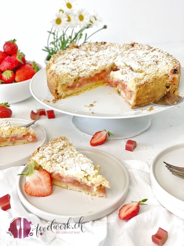 streuselkuchen mit erdbeeren und rhabarber auf weiser kuchenplatte serviert