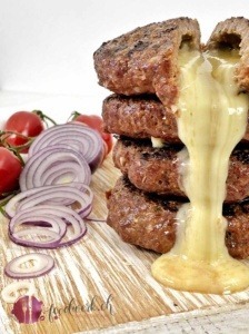 MIt Raclette Suisse gefüllte Rinds Burger, aufgeschnitten auf einem hellen Holzbrett und der Käse läuft aus den Burgern