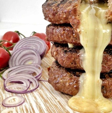 MIt Raclette Suisse gefüllte Rinds Burger, aufgeschnitten auf einem hellen Holzbrett und der Käse läuft aus den Burgern