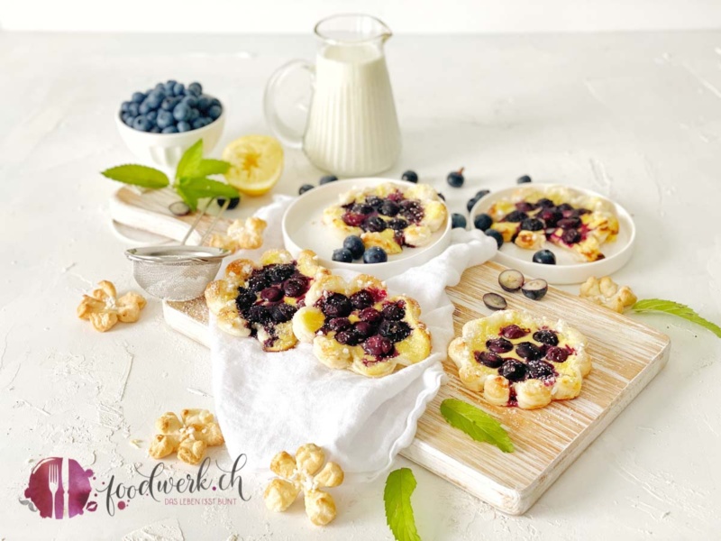 Blätterteig Blume mit Blaubeeren auf weissem Tuch und hellem Holzbrett