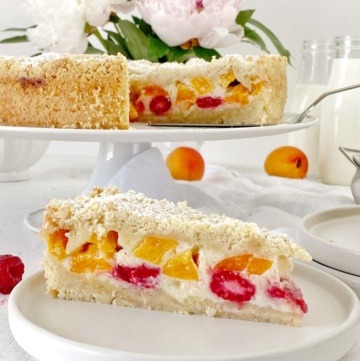 Streuselkuchen mit Aprikosen und Himbeeren auf weiser Tortenplatte mit Tortenschaufel