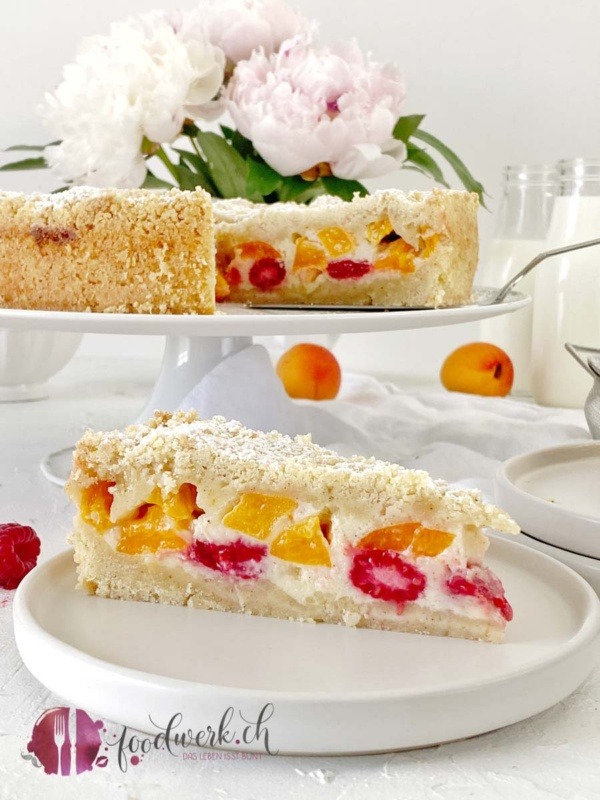 Streuselkuchen mit Aprikosen und Himbeeren auf weiser Tortenplatte mit Tortenschaufel