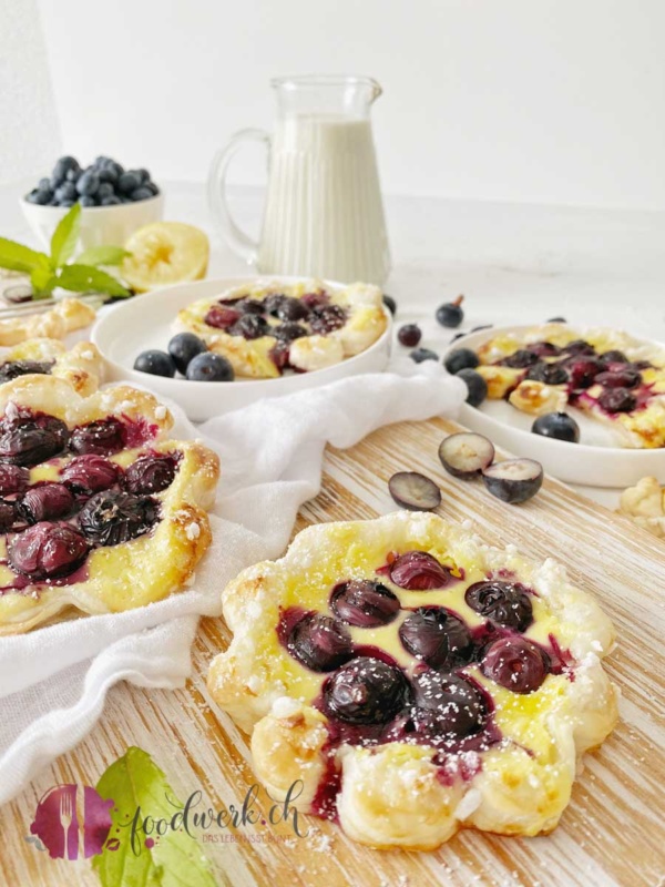 saftige Blaubeeren auf Quarkmasse mit Blätterteig Blume auf hellem Holzbrett