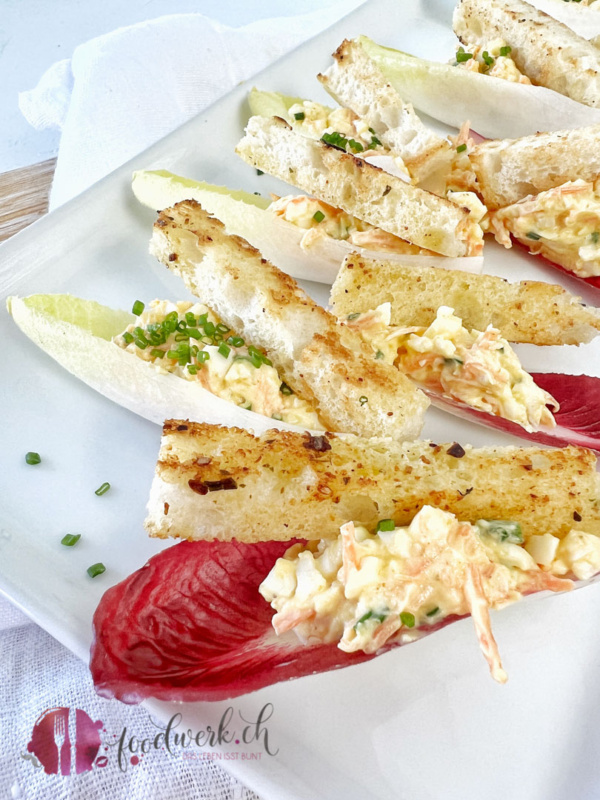 Chicorée Schiffchen auf weissem Teller mit knusprigen Brotsticks