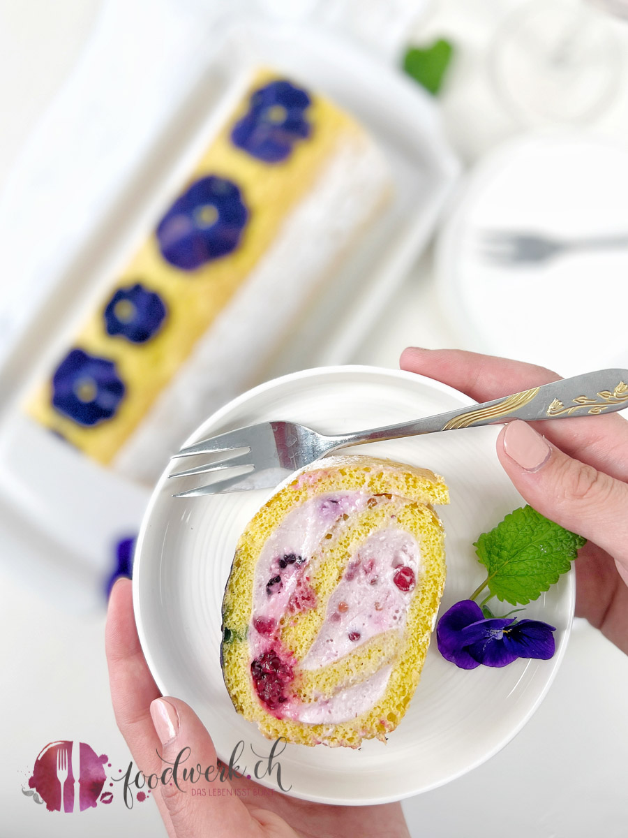 Roulade mit Beerencreme und Blüten auf weissem Teller