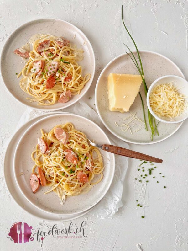 Zwei Teller mit Spaghetti und Cervelat mit Schnittlauch und geriebenem Sbrinz